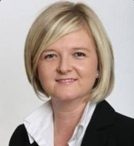 A woman with blonde hair is wearing a black jacket and white shirt.