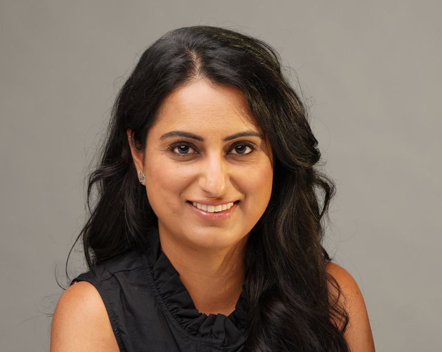 A woman with long dark hair is smiling and wearing a black shirt.