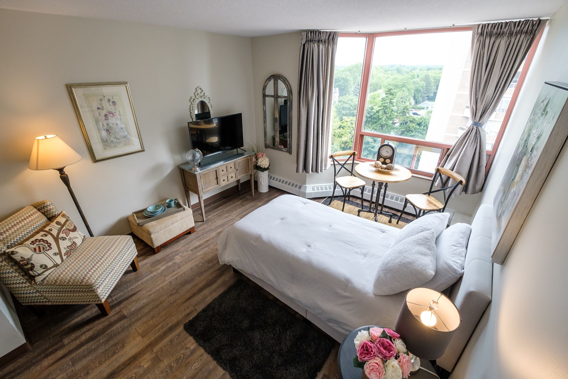 A bedroom with a bed , chairs , a table and a large window.