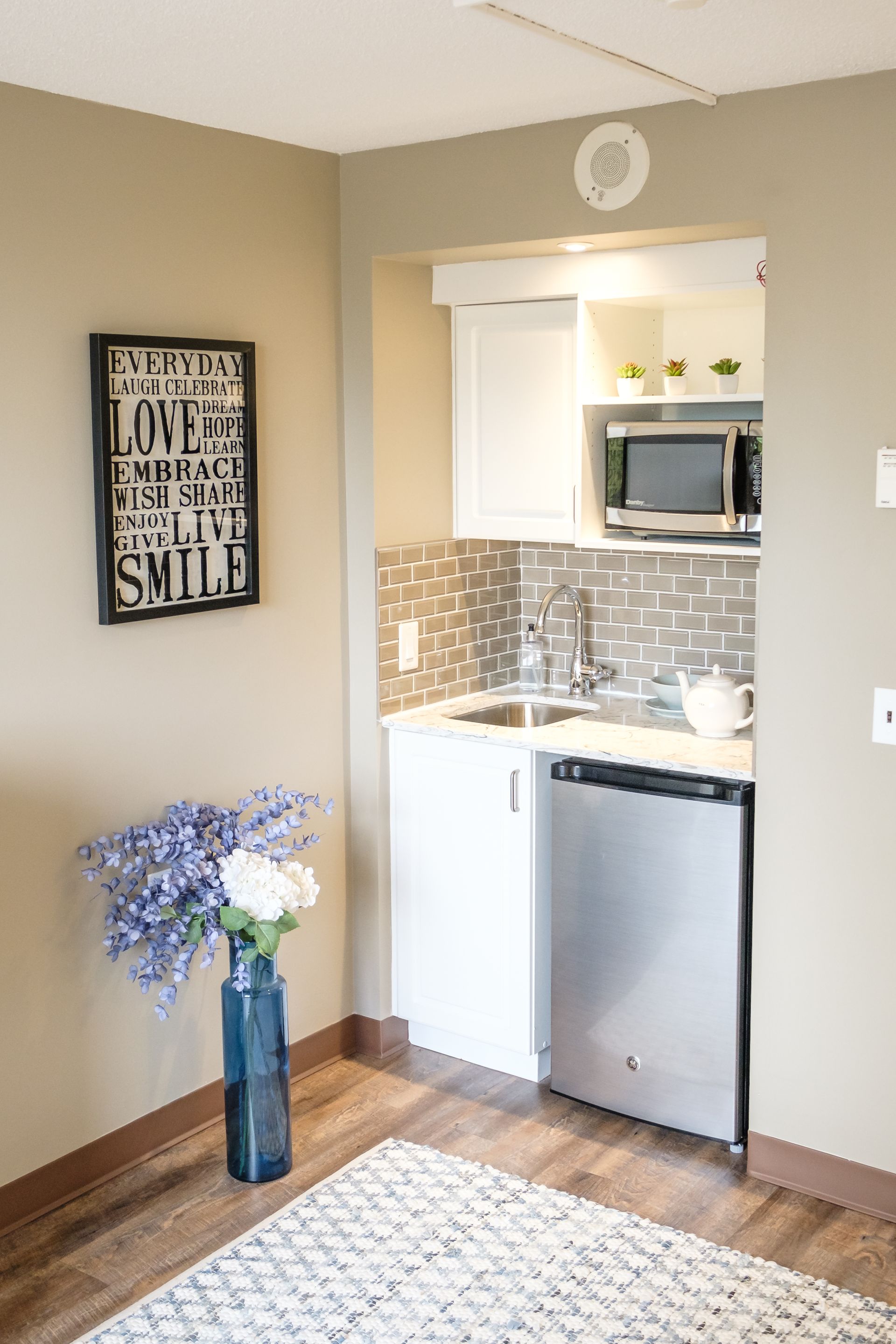 A kitchen with a sink , dishwasher , microwave and a vase of flowers.