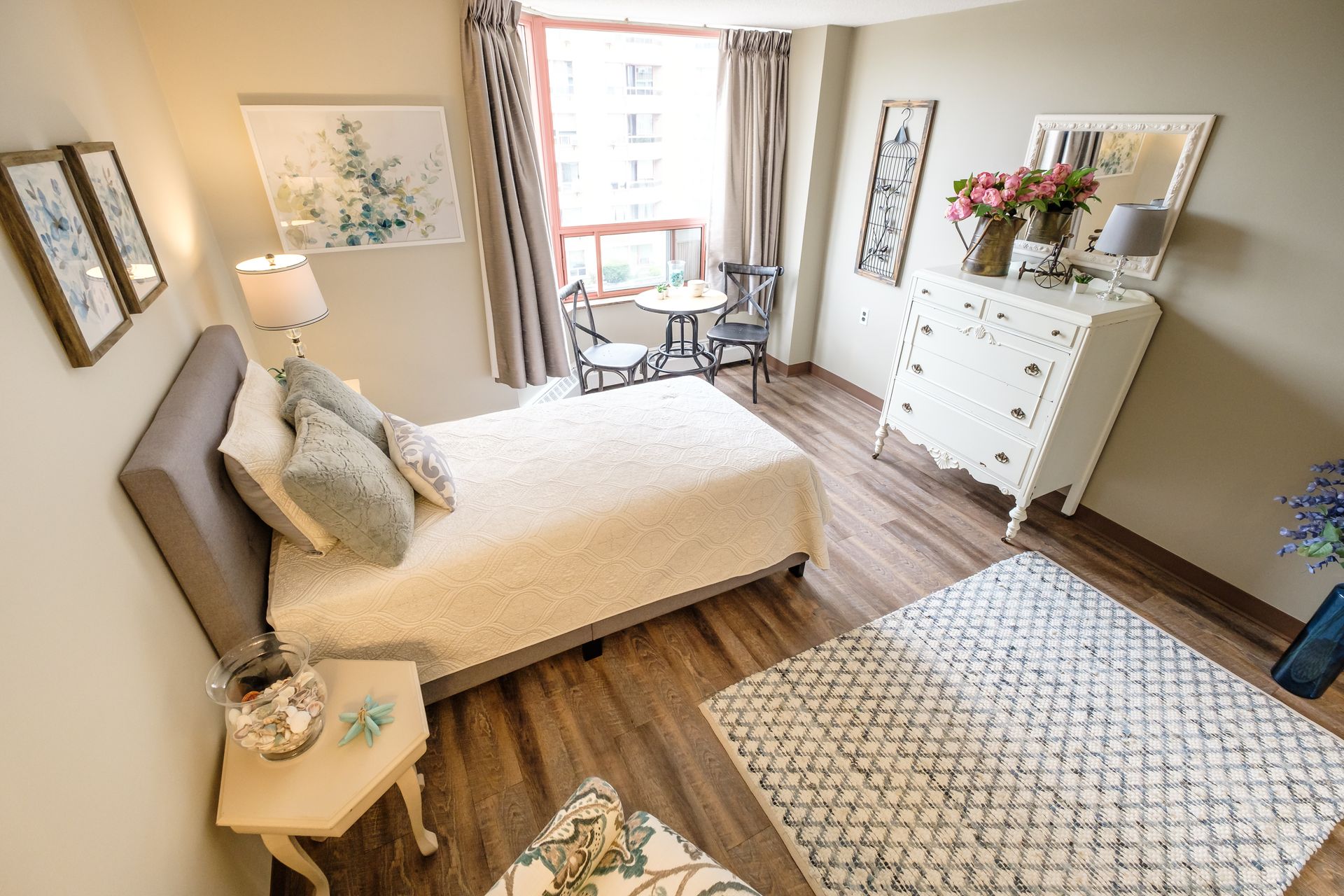 A bedroom with a bed , dresser , table and chairs.