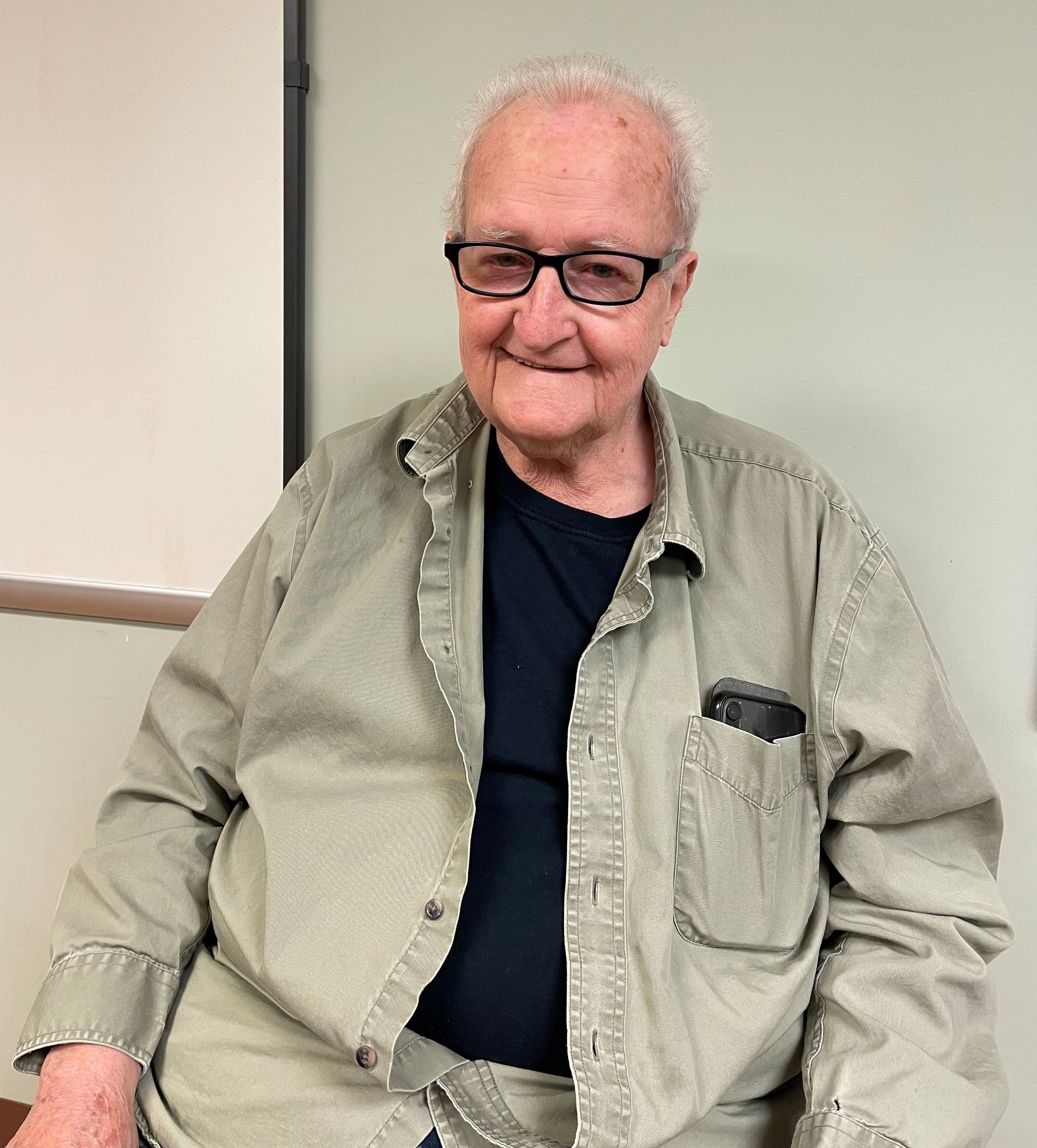 Woman seated in a blue armchair wearing a purple sweater and pink shirt; smiling, indoors.