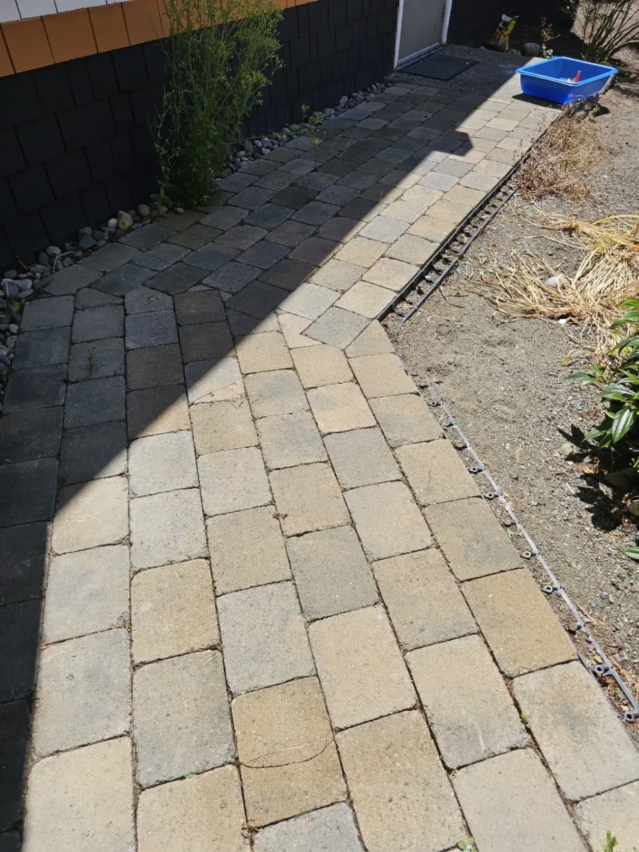 Stone paver pathway with a slight incline, alongside a black fence and gravel bed.