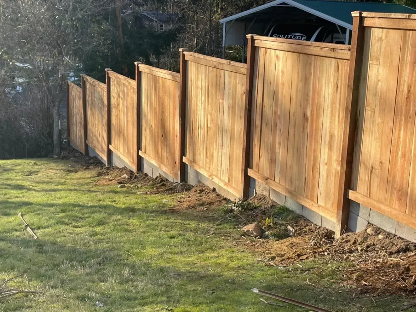 Wooden fence along a grassy yard. The fence is made of light brown wood panels, in a residential setting.