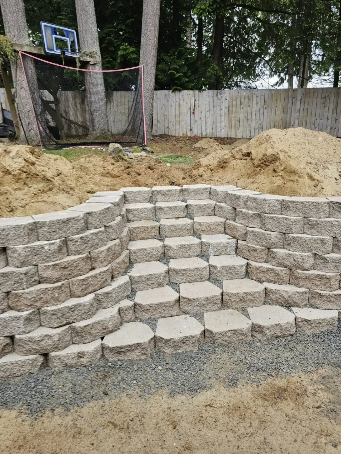 Stone retaining wall steps built in a backyard, with sand and gravel in the foreground.