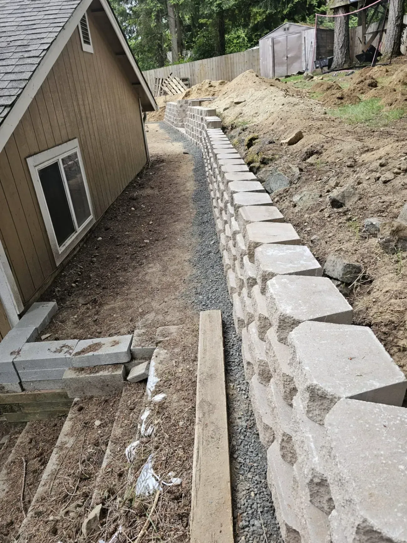 A retaining wall constructed of gray blocks next to a building and a sloped yard.