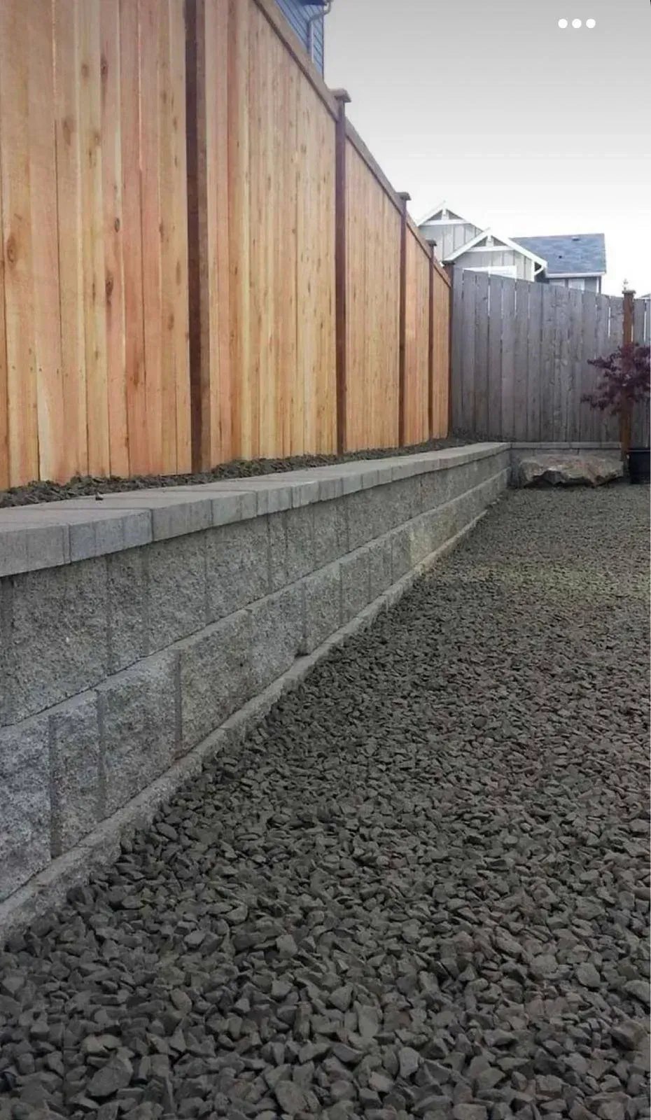 A cedar fence atop a gray retaining wall, gravel ground.