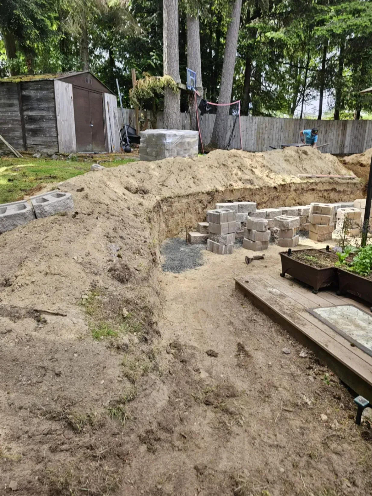Construction site: excavation with cinder blocks, sand, and wooden planks outdoors.