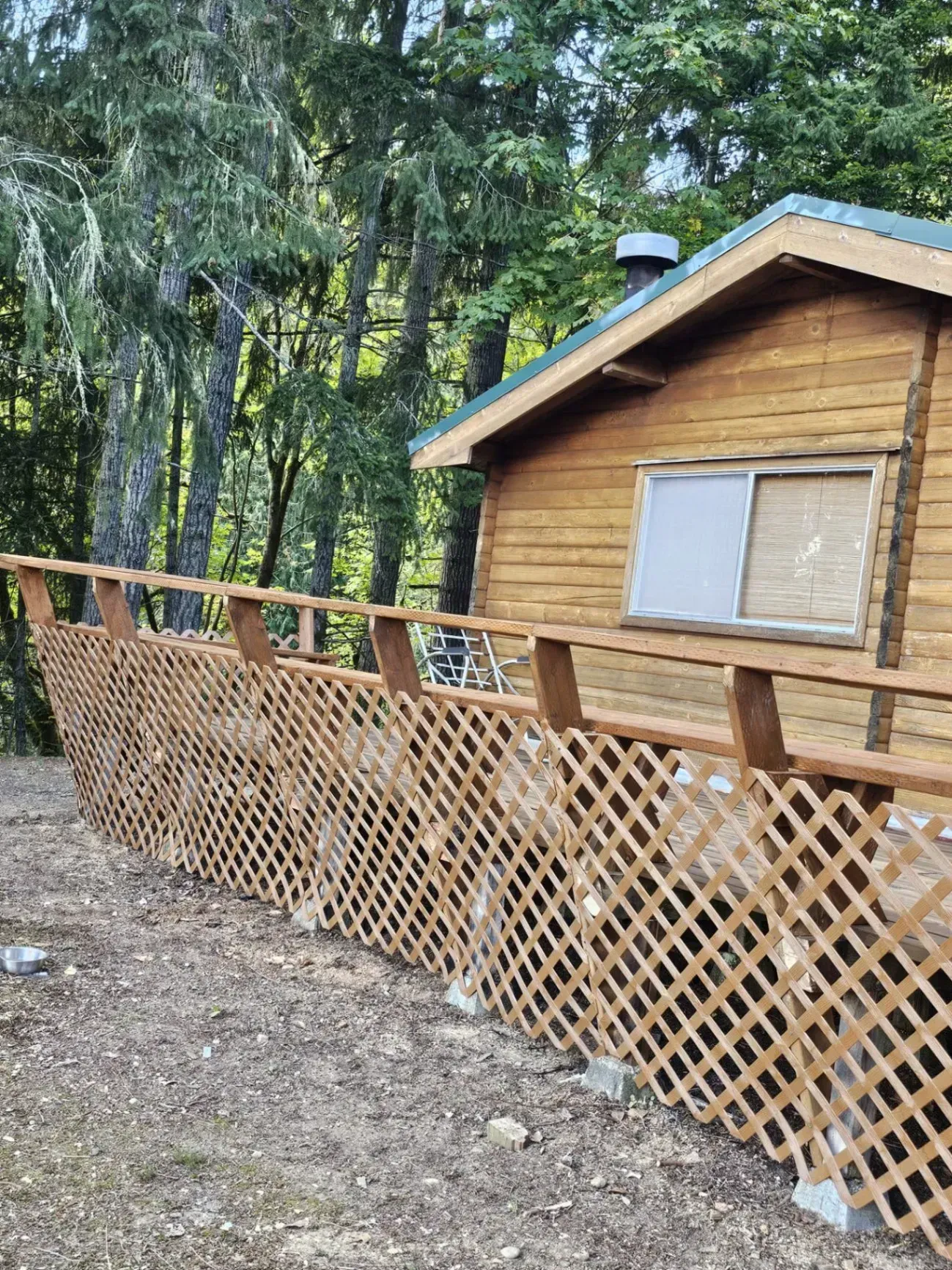 Wooden cabin with latticework railing, set in a wooded area.