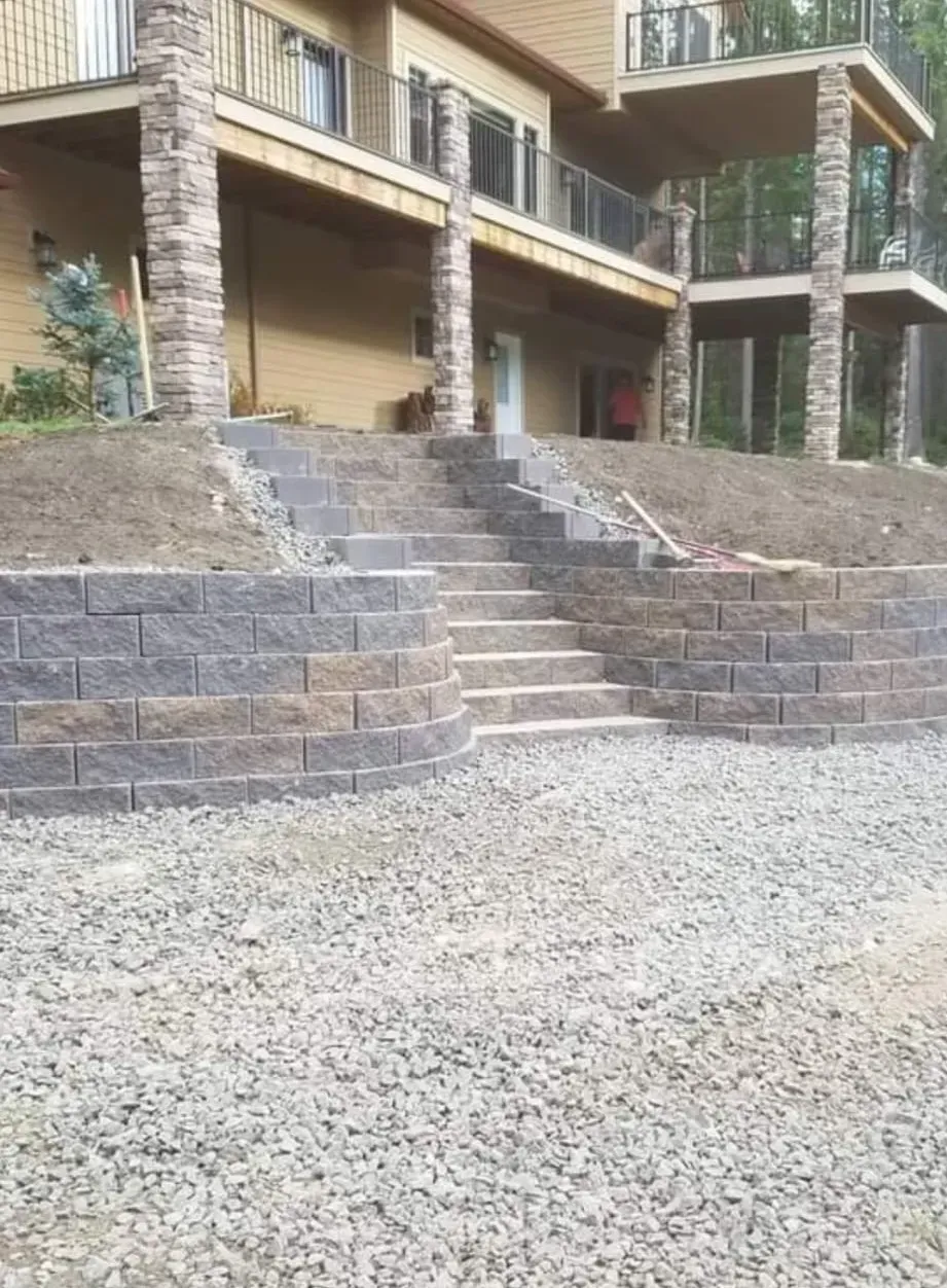Stone retaining wall with steps leading to a house with a balcony. Gravel in the foreground.