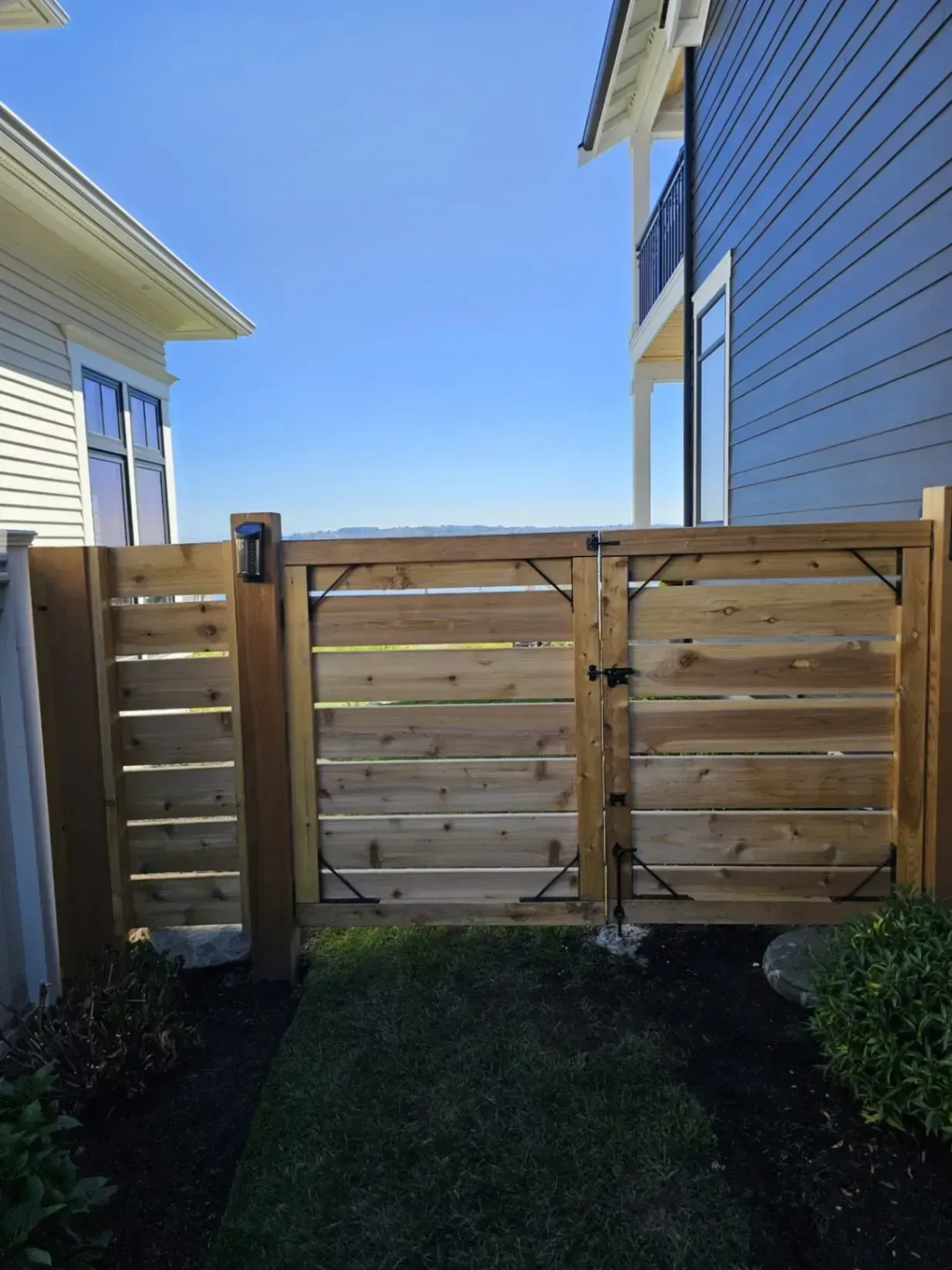 Wooden gate in a yard, between two buildings, with a blue sky above.
