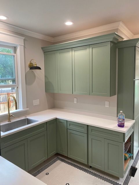 A kitchen with green cabinets , a sink , and a window.