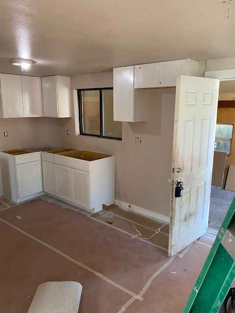 A kitchen under construction with white cabinets and a green ladder.