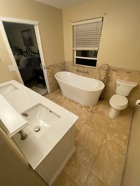 A bathroom with a tub , sink , toilet and window