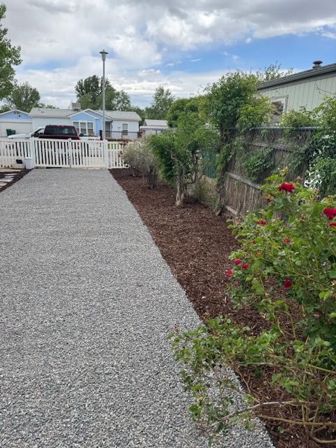 A gravel driveway leading to a house with a fence and flowers.