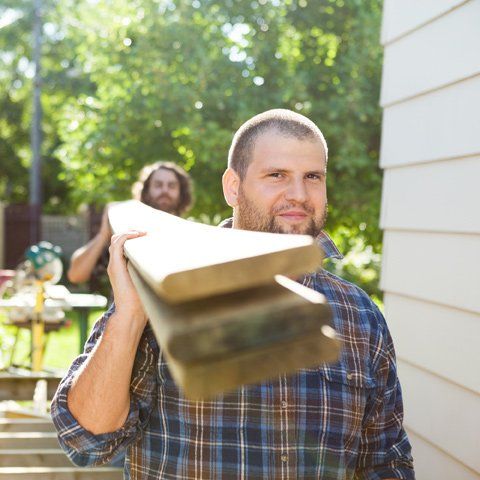 A man in a plaid shirt is carrying a stack of wood