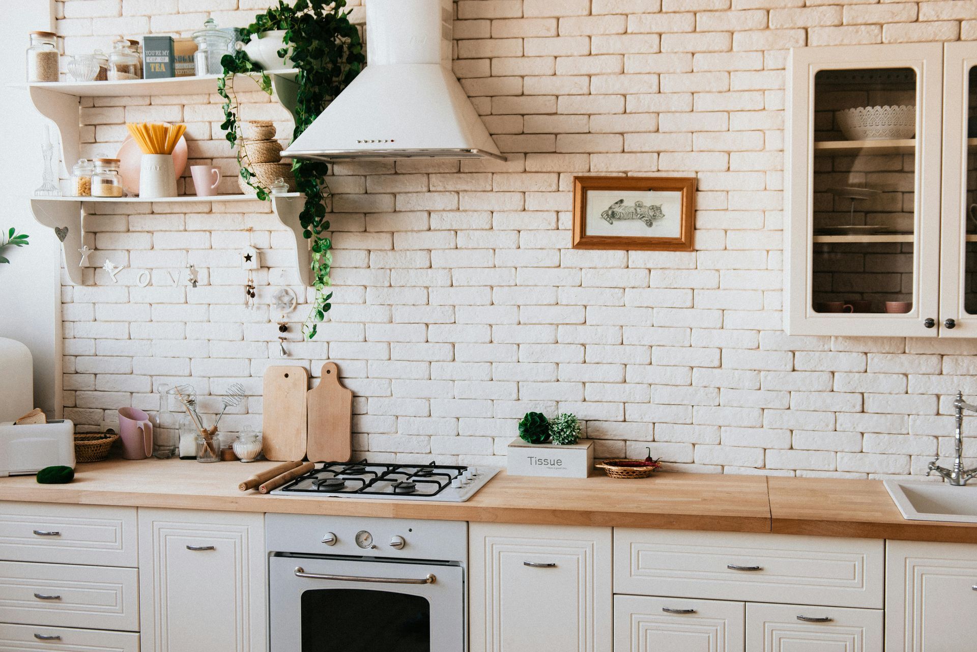 A kitchen with white cabinets , a stove , a sink , and a brick wall.