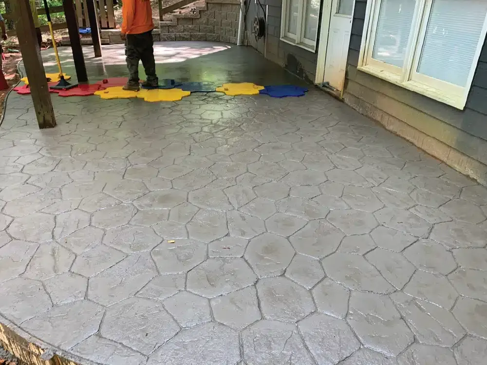 A worker laying down the mold for a stamped concrete back patio that is almost complete.