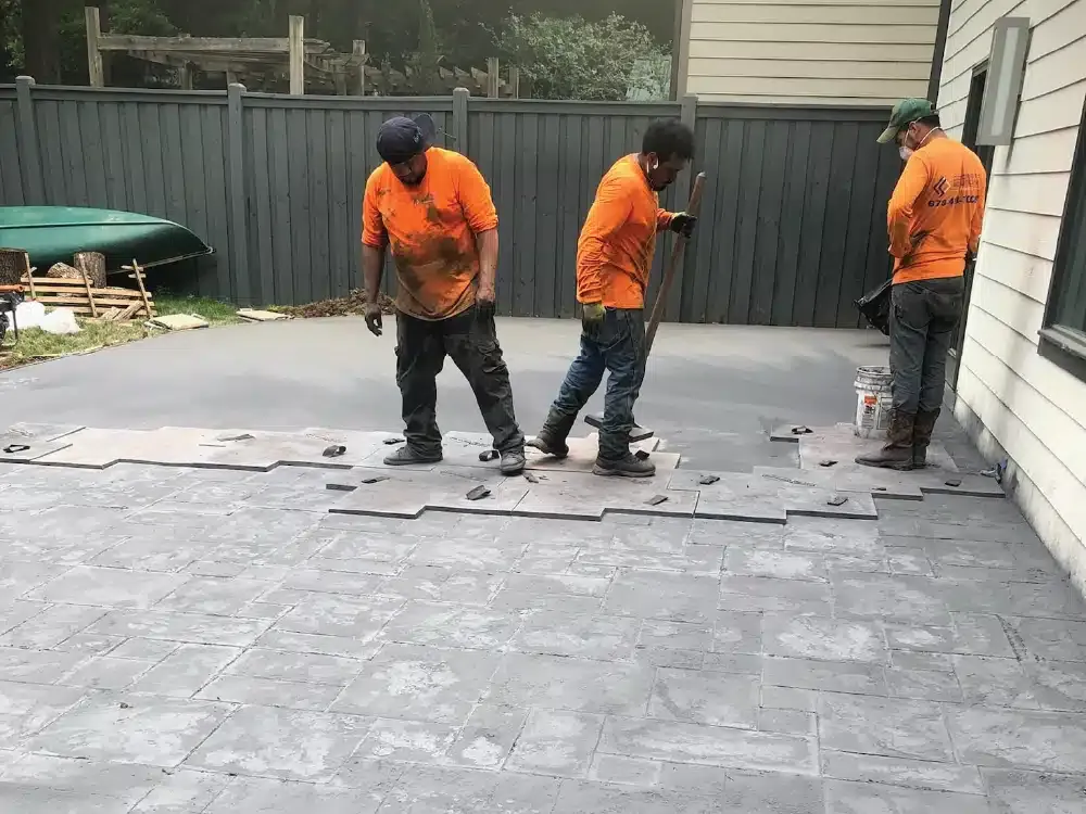 Three men are working on a concrete patio in front of a house.