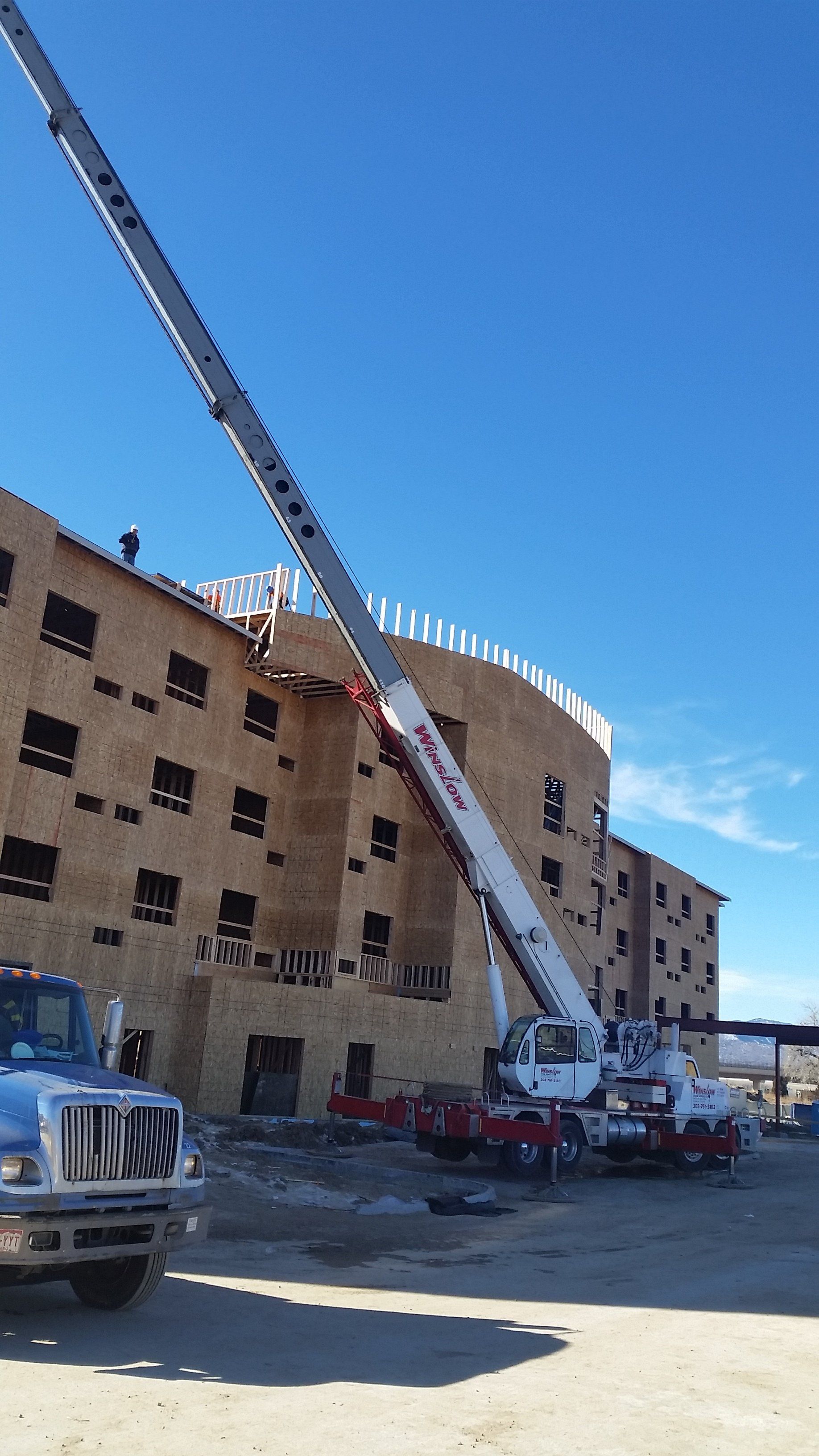a truck with a crane attached to it is parked in front of a building under construction .