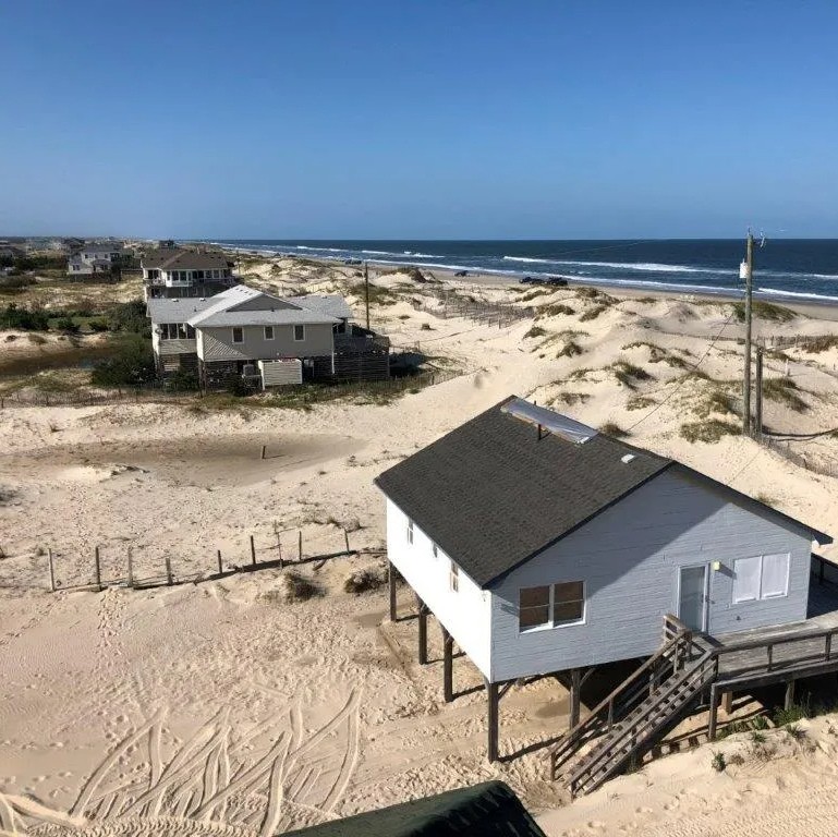 a small white house on stilts on a sandy beach