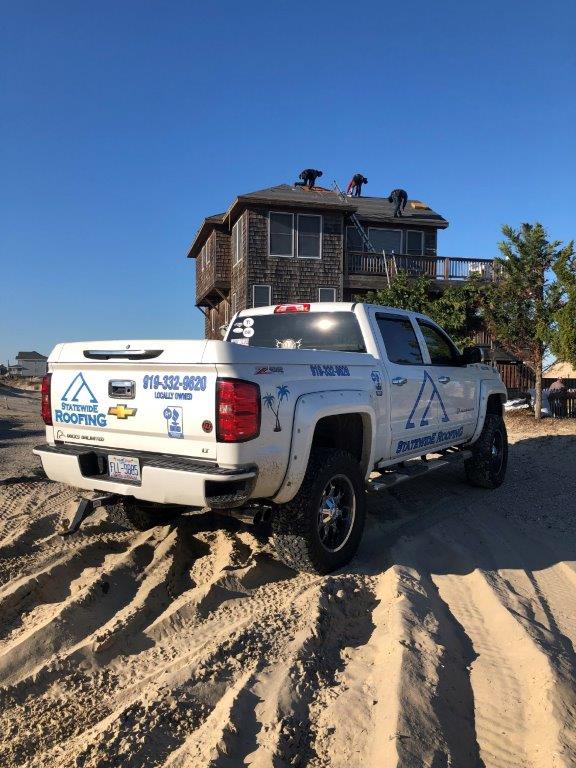 a white truck is parked in the sand in front of a house .