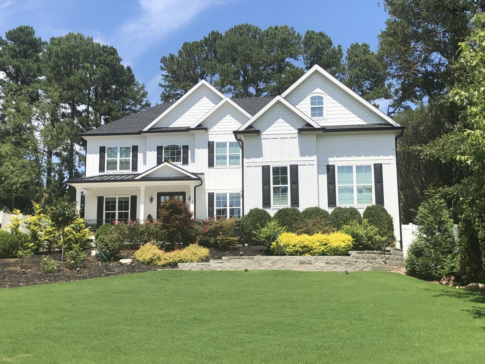 a large white house with black shutters sits on top of a lush green hillside