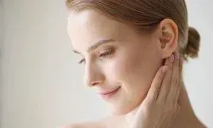 Woman with fair skin, touching her neck, eyes closed in a gentle pose.