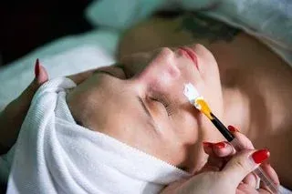 Woman getting a facial, white cream applied with brush; spa setting.