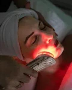 Woman receiving red light therapy on her face at a spa. She is laying down with eyes closed.