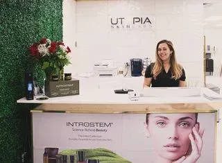 Woman at a cosmetic business counter; green wall backdrop, roses and products present.