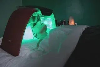 Person receiving green light therapy on their face while lying down on a spa bed.
