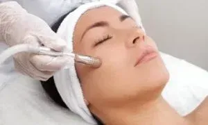 Woman receiving microdermabrasion treatment at a spa, white headband, closed eyes.