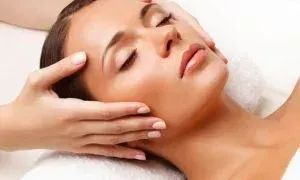Woman receiving a facial massage with hands on her face; eyes closed in relaxation.
