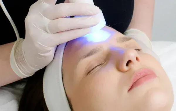 Woman receiving blue light therapy treatment on her forehead in a salon.