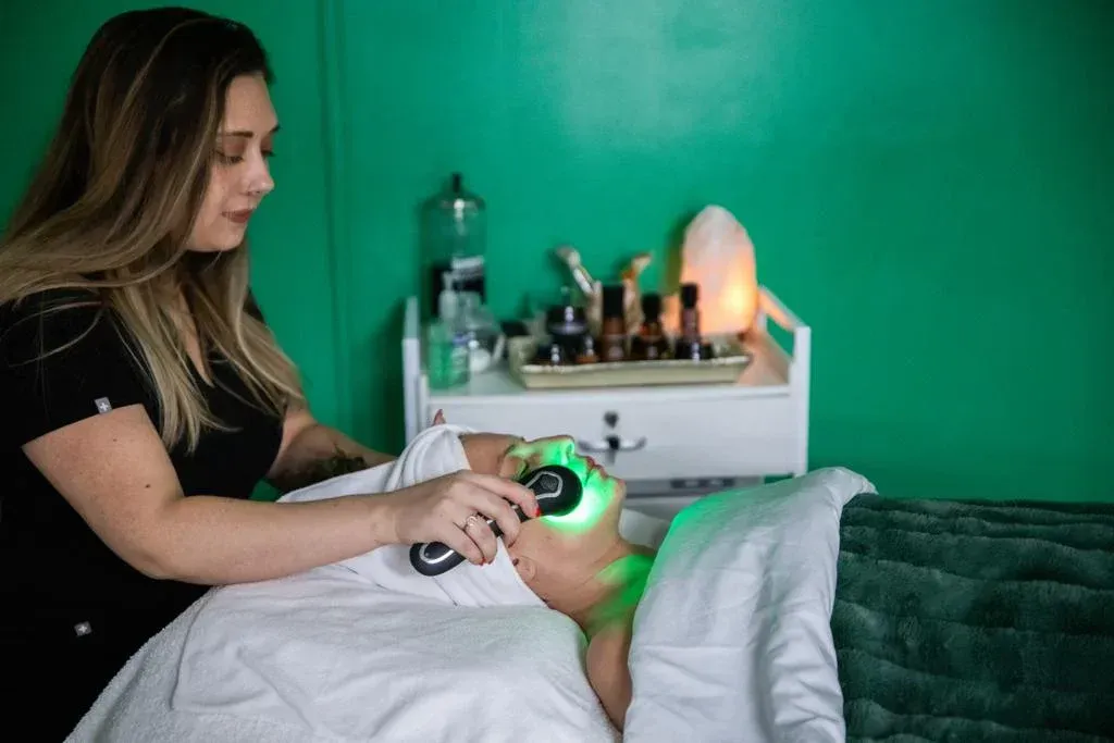 Woman giving client a facial with green light therapy in a spa setting.