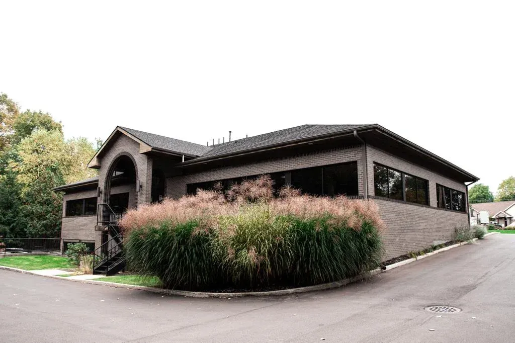 Restaurant exterior with gray stone walls, large windows, and tall ornamental grasses.