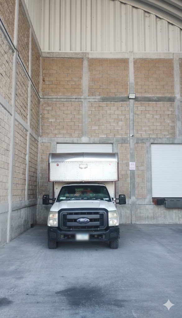 Camión estacionado en reversa en el muelle de carga de un almacén, mirando hacia adelante. Edificio gris y canela.
