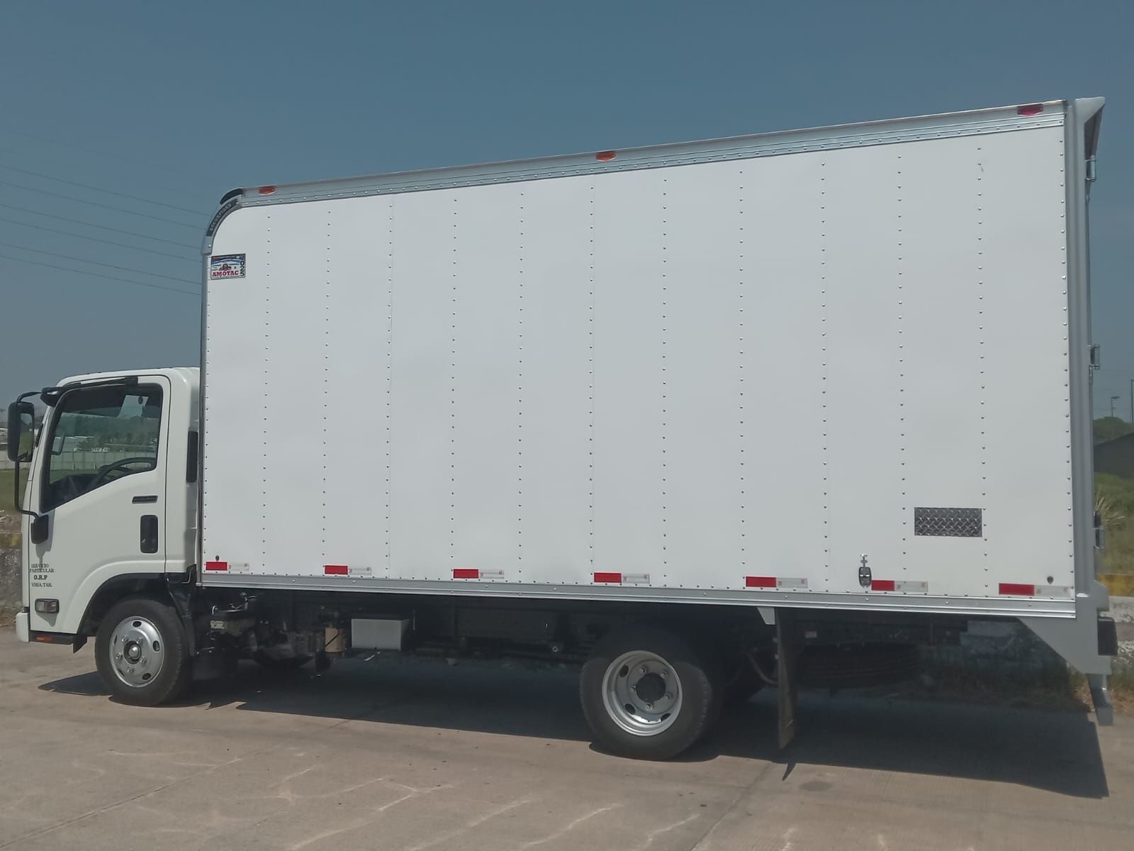 Camión de caja blanca estacionado sobre la acera contra un cielo brillante.