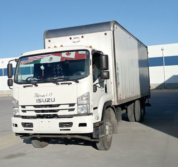 Camión de caja blanca circulando por una carretera pavimentada, bajo un cielo azul claro.