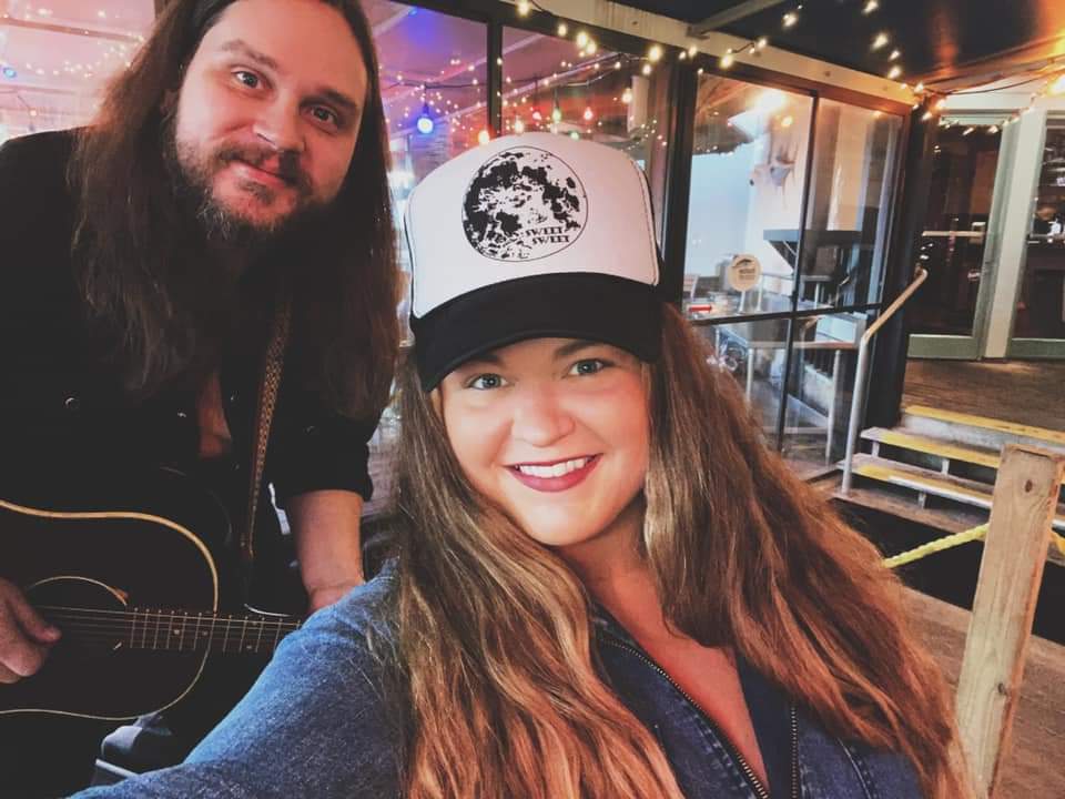 A man is playing a guitar next to a woman wearing a hat.