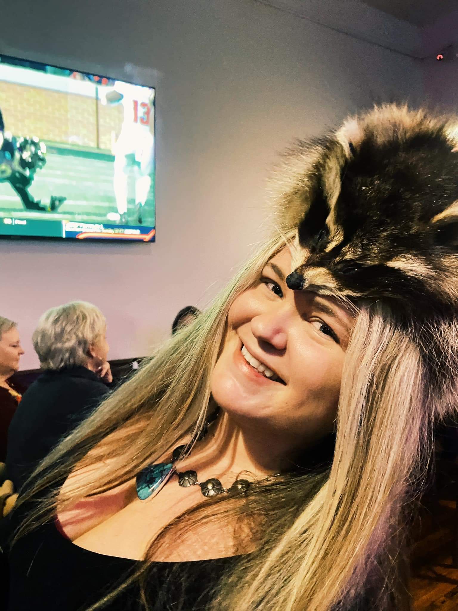 A woman wearing a raccoon hat with a raccoon on her head.
