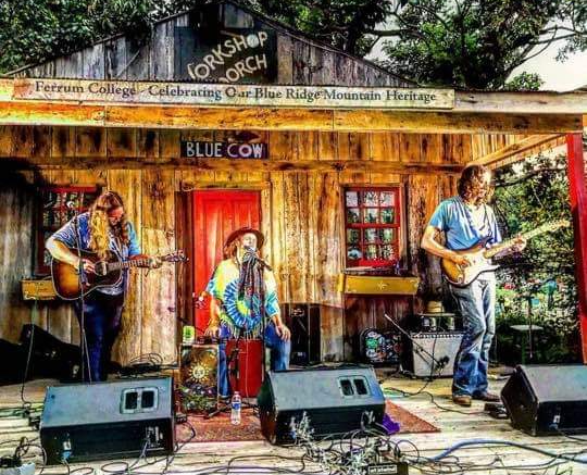 A group of people are playing instruments on a stage in front of a wooden building.