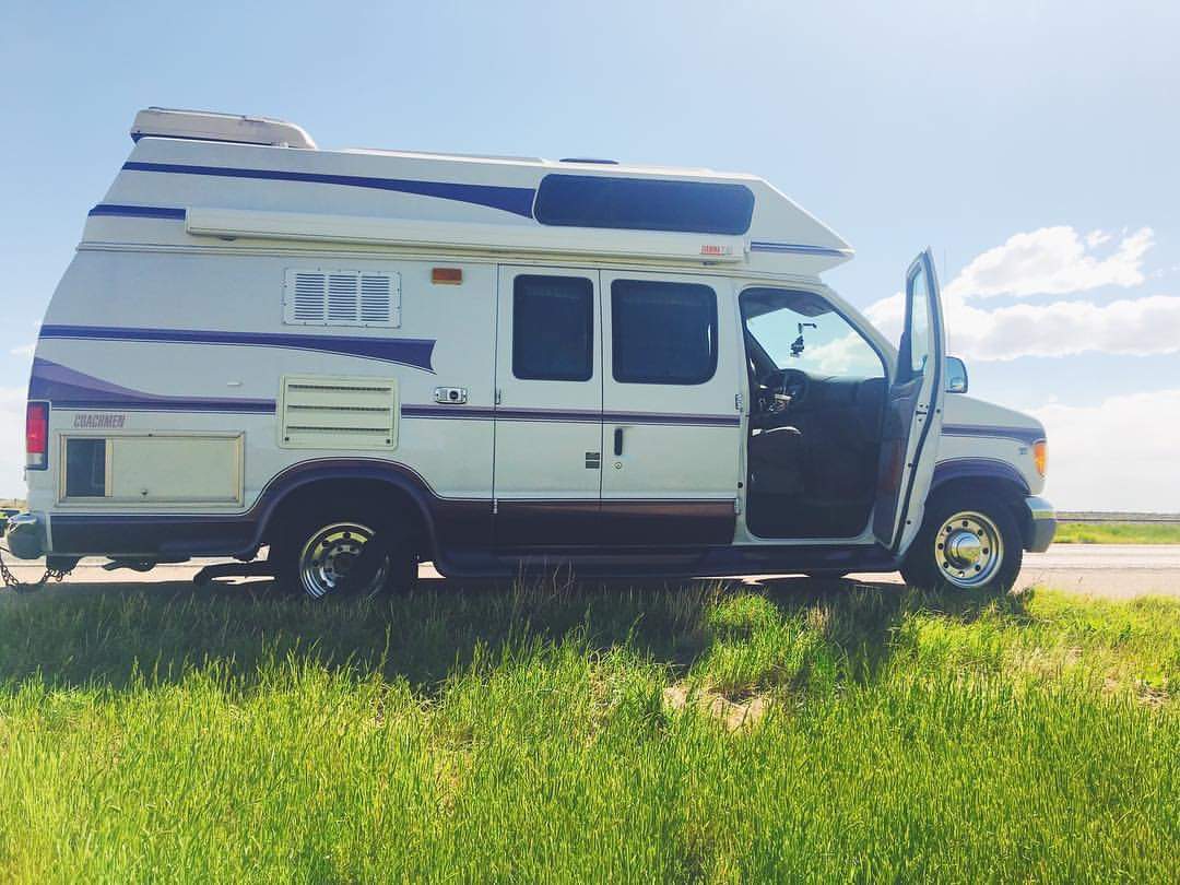 A white van is parked in a grassy field on the side of the road.