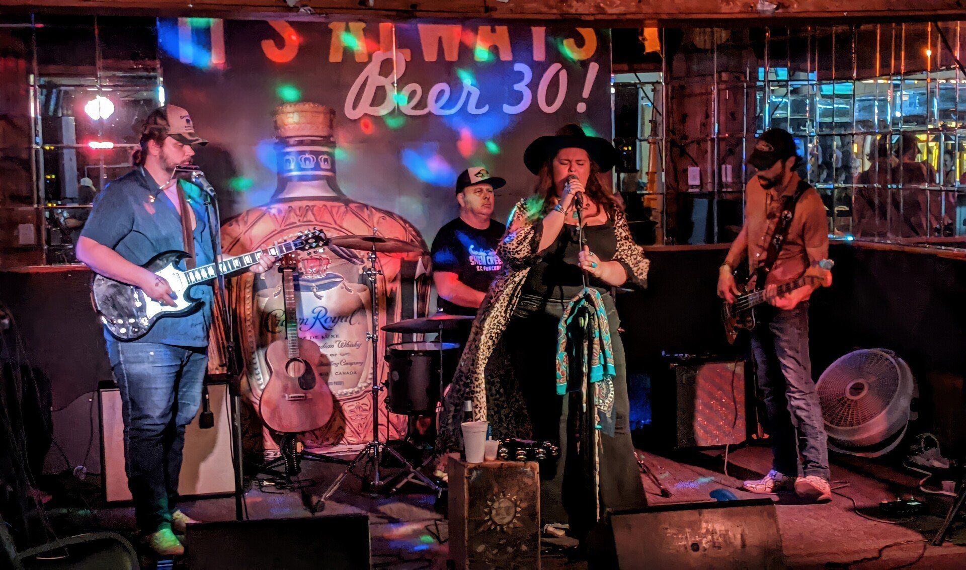 A group of people are playing instruments on a stage in front of a sign that says beer 30.