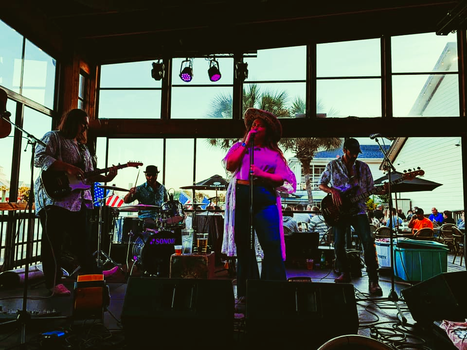 A woman is singing into a microphone while a band plays instruments on stage.