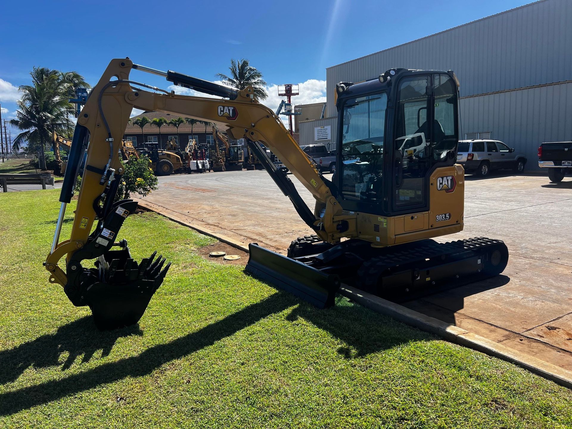 A yellow Caterpillar mini excavator with a black bucket and rubber tracks parked on grass next to a gravel lot.