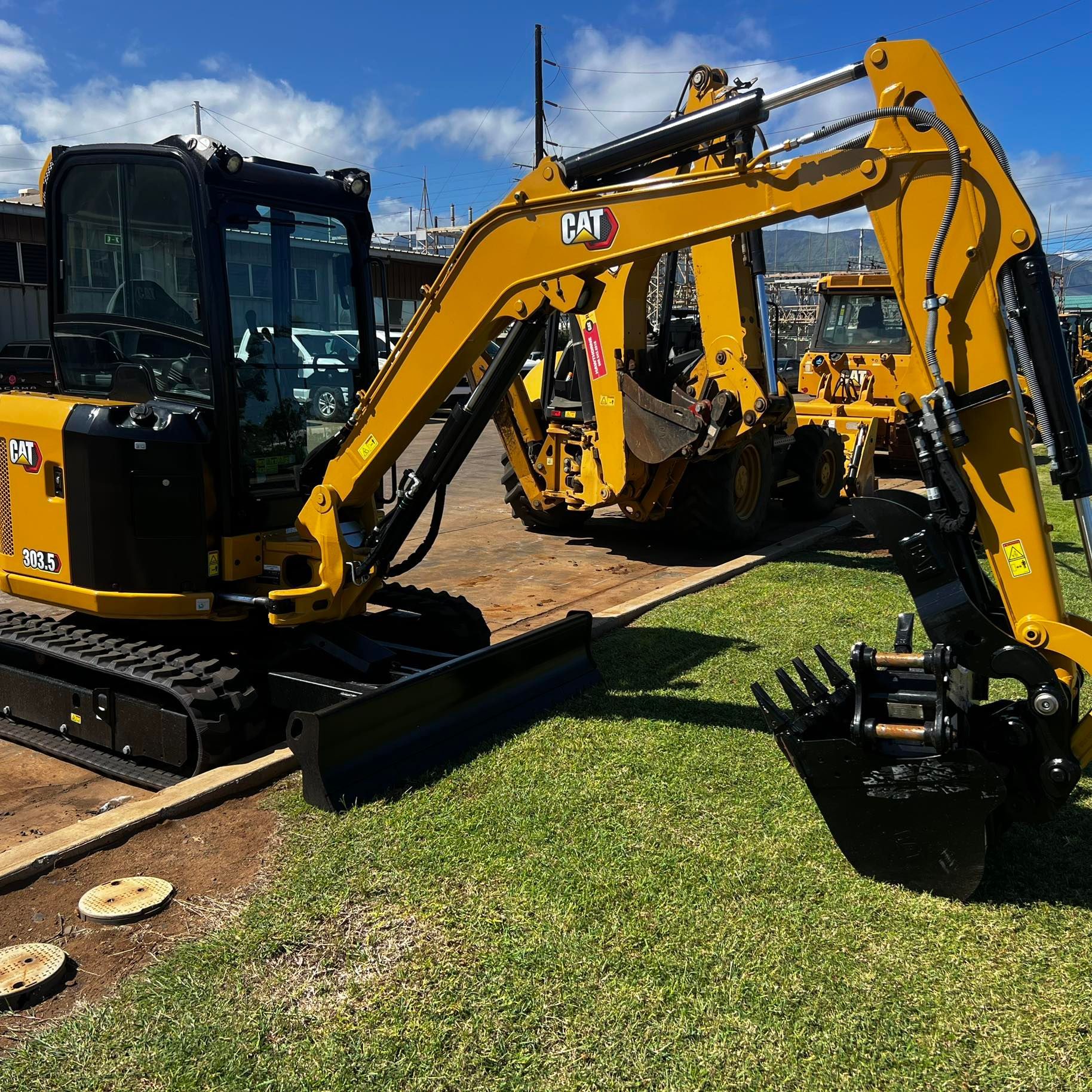 A yellow Caterpillar 314 mini excavator parked on a grassy lot with another piece of heavy machinery in the background.