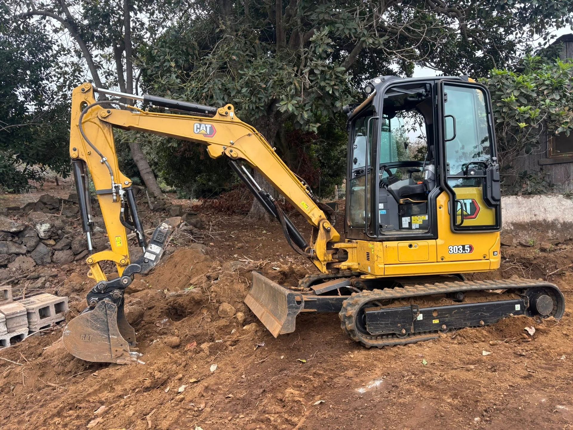 A yellow Caterpillar mini excavator sits on a dirt construction site with a raised blade and bucket positioned on the ground.