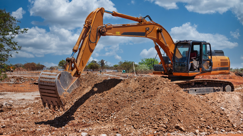 An orange excavator digging into a pile of dirt at a sunny construction site under a blue sky with clouds.